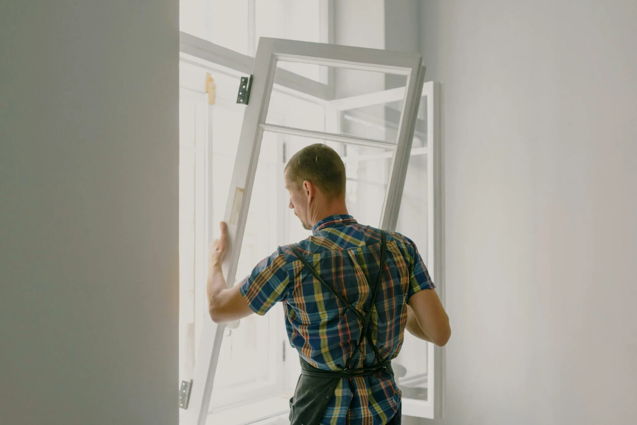 Ein Handwerker in kariertem Hemd und Schürze installiert ein Fenster in einem Innenraum